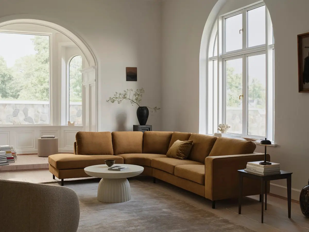 Living room with a mustard corner sofa, round table and large arched windows