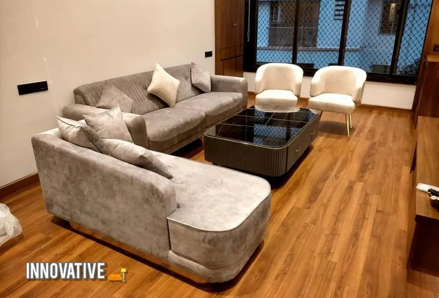 Grey L-shaped sofa with a dark coffee table and two cream chairs on a wooden floor