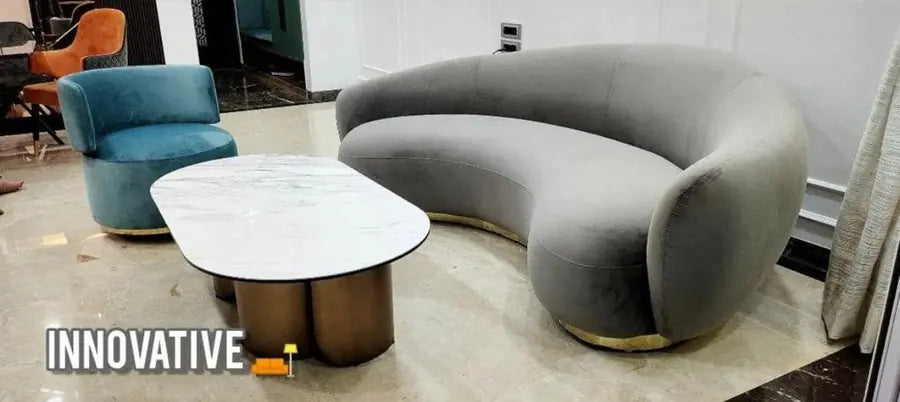 Grey curved sofa with a marble-top coffee table and a teal accent chair