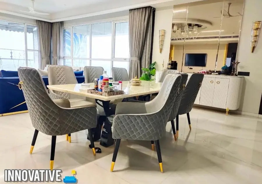 Marble-top dining table with grey quilted chairs with gold feet