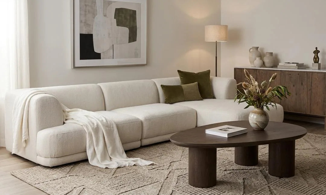 Cream modular sofa with a throw blanket, olive cushions and an oval walnut coffee table