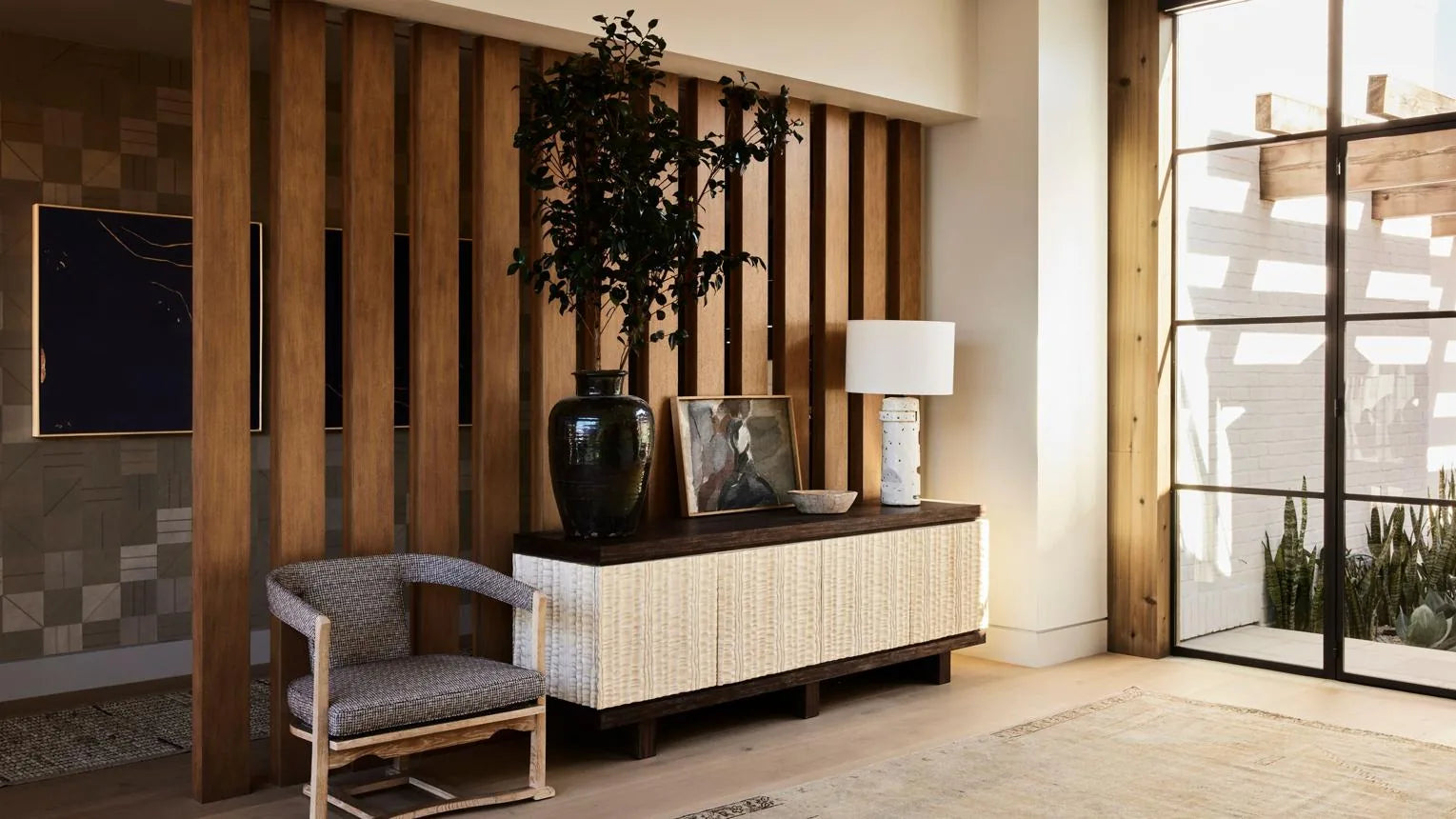 Oak entryway sideboard with a dark vase, a slatted wood divider and a woven accent chair